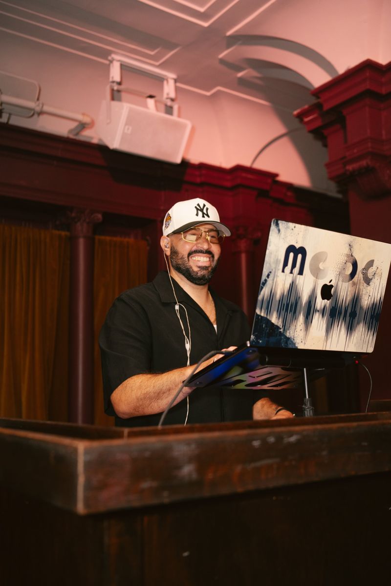 DJ Mode at a wooden podium with his laptop