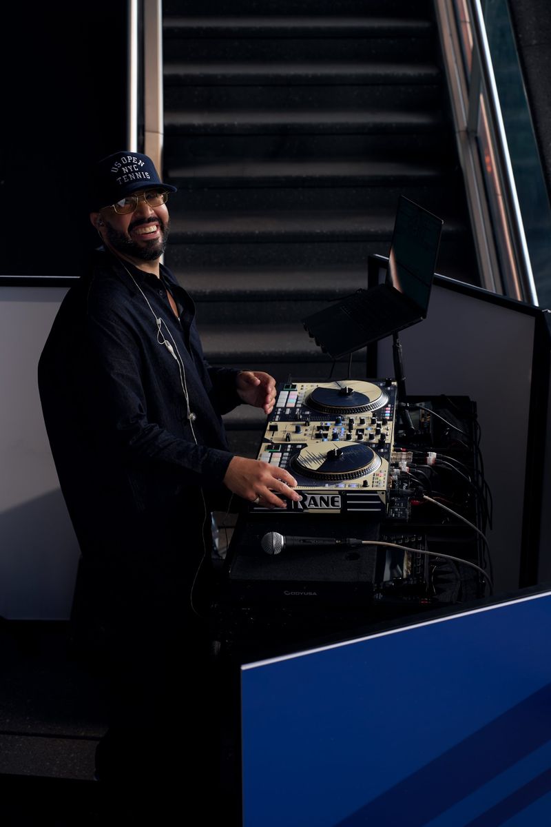 DJ Mode smiling at his Rane decks in a US Open NYC Tennis cap