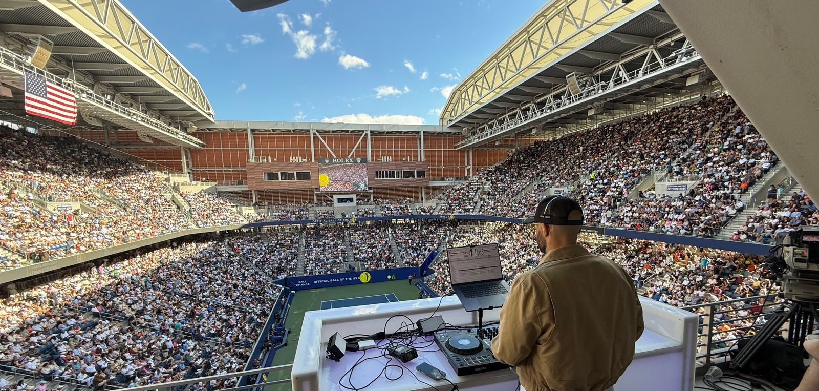 View over the shoulder of DJ Mode at the decks above a packed US Open stadium